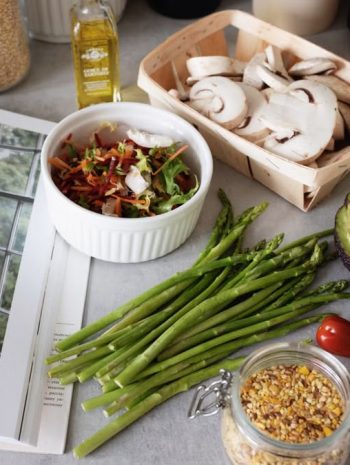 A selection of fresh vegetables and a cookbook in a kitchen setting, promoting healthy cooking.