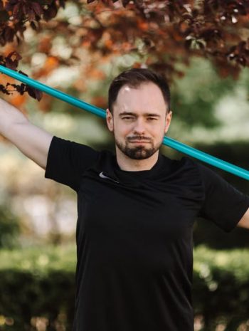 Adult man in black shirt exercises with a resistance band outside.