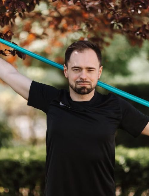 Adult man in black shirt exercises with a resistance band outside.